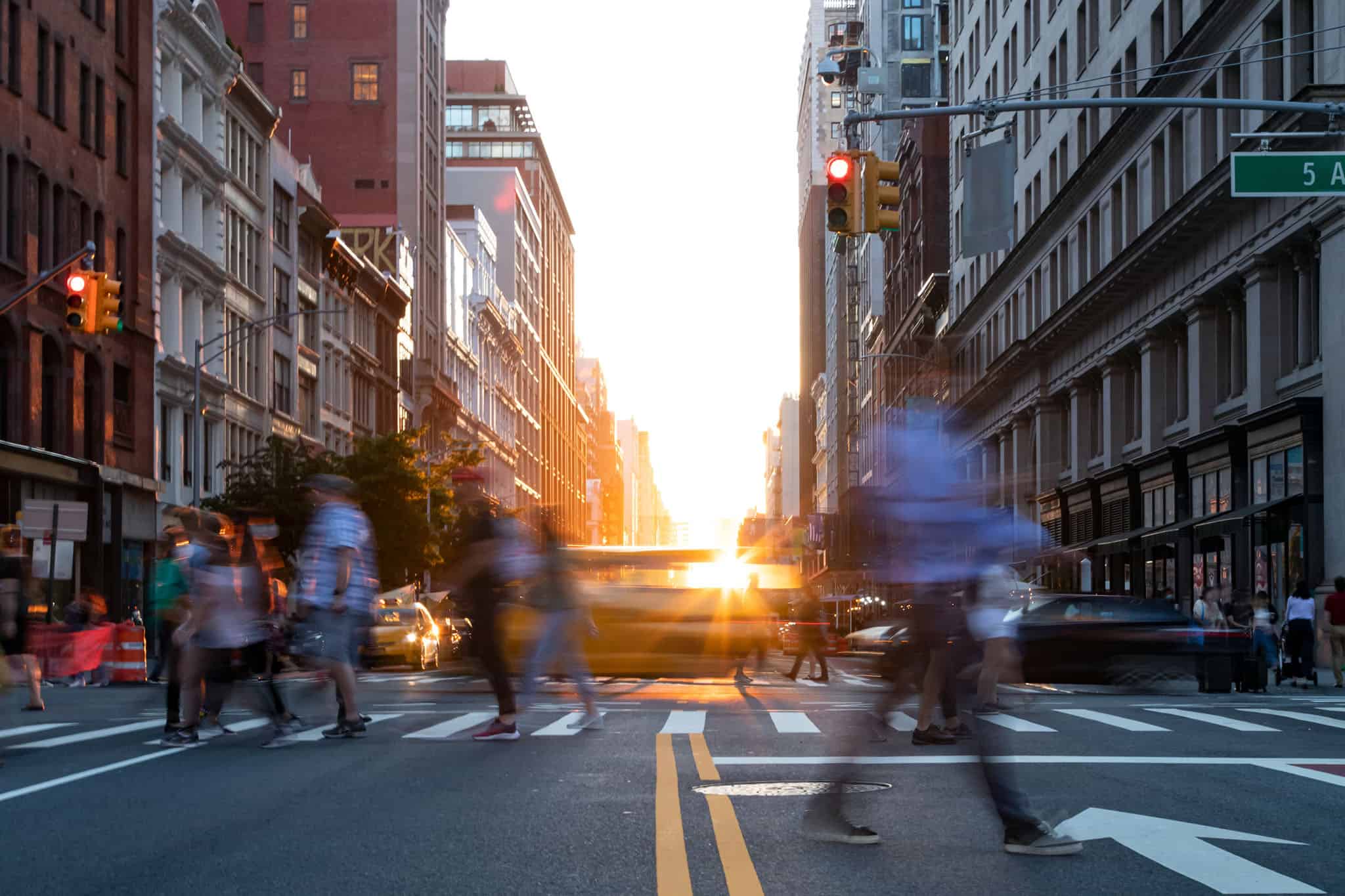 Busy street intersection is crowded with people and cars on 5th Avenue in Manhattan New York City with sunlight background